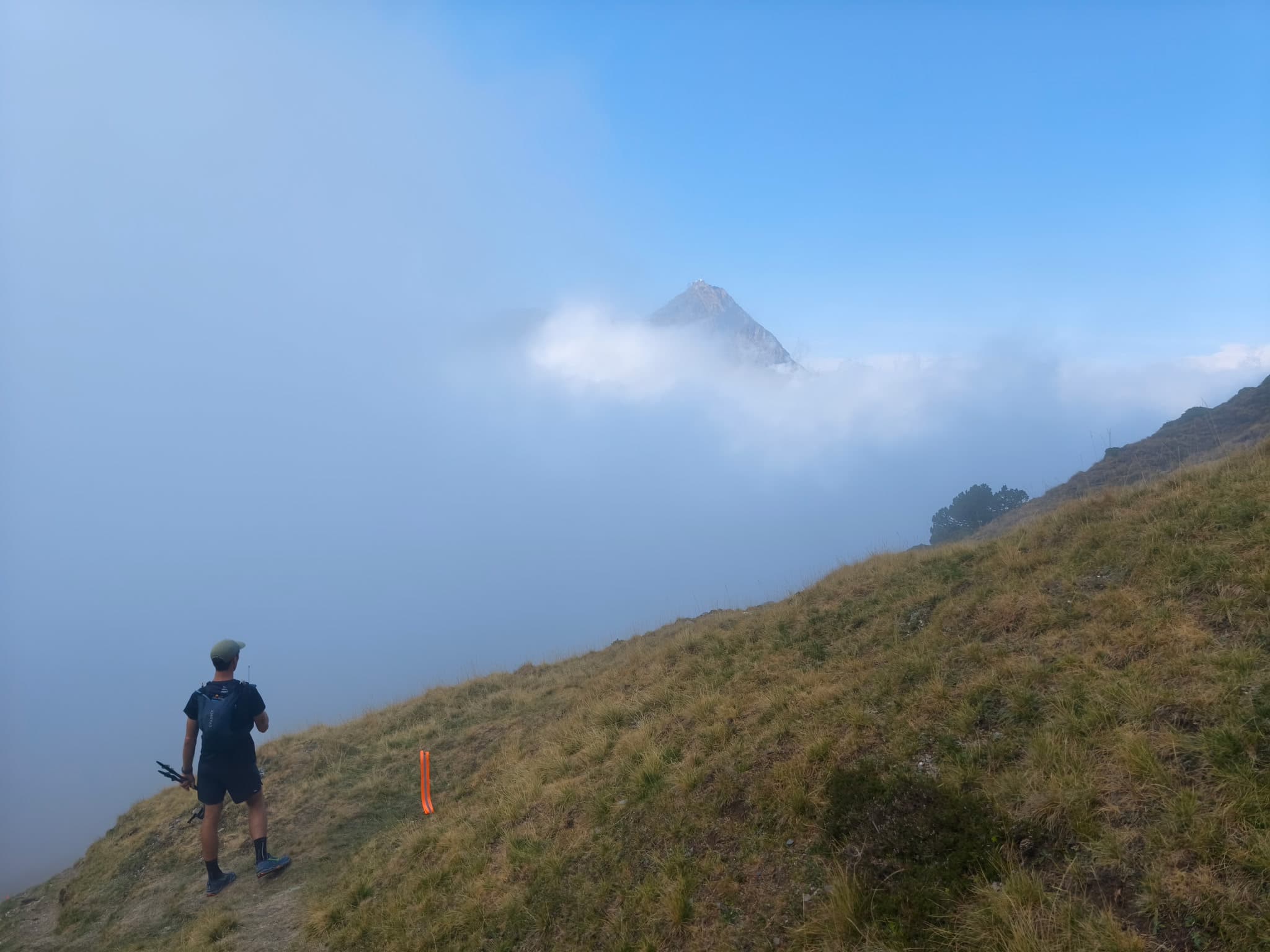 Loïc Simon sur un sentier de crête au-dessus d'une mer de nuages, balise de circuit au premier plan