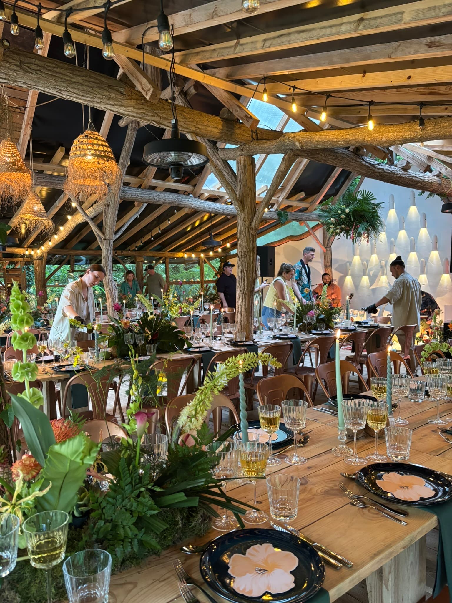 Long tables laid under a timber frame, crew finishing the set-up